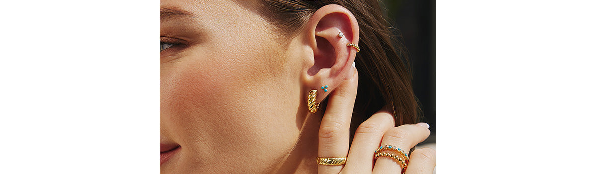 Close up of earring stack featuring clean and modern gold hoop, stud, and sparkly ear cuff.
